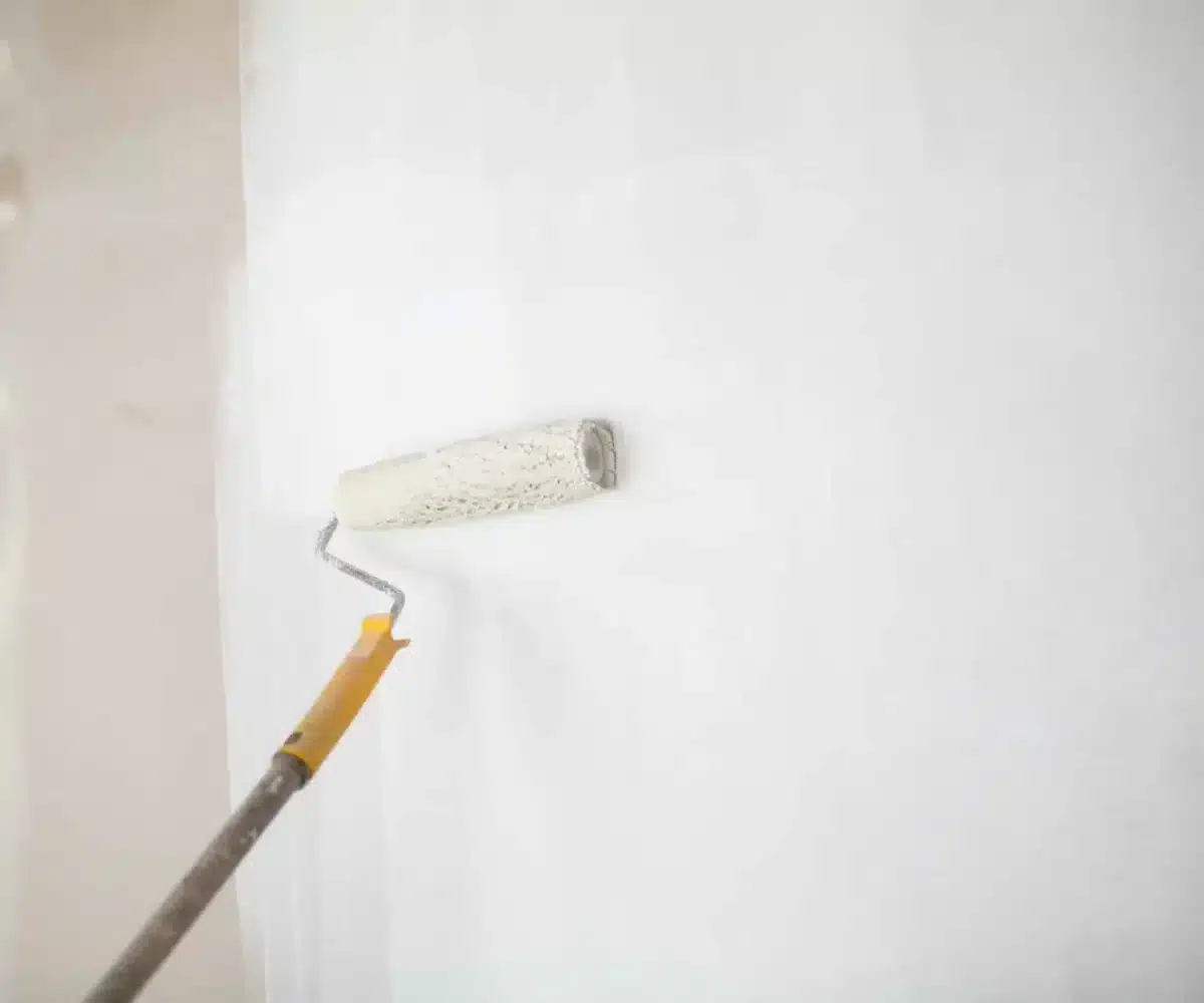 white-paint-roller-in-hand-with-drywall-wall-painting-scaled